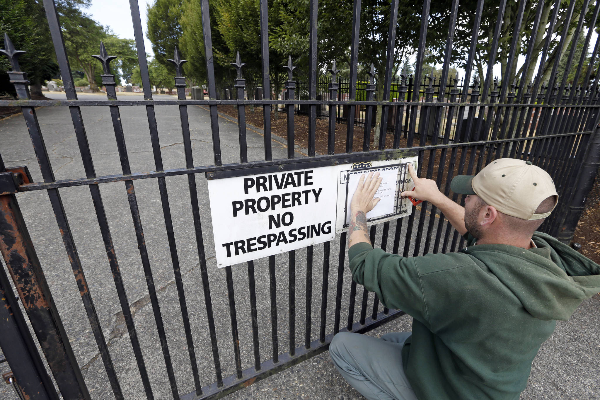 A worker, who declined to be identified, posts a notice of temporary closure on the locked gates of Lake View Cemetery in Seattle, which was shut Thursday following angry messages it’s received over a memorial for Confederate soldiers. (Elaine Thompson/The Associated Press)