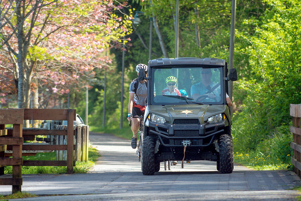 Cyclists follow behind as Clallam County Sheriff’s Deputy Mike Leiter patrols the Olympic Discovery Trail near Hollywood Beach in Port Angeles on Thursday. (Jesse Major/Peninsula Daily News)