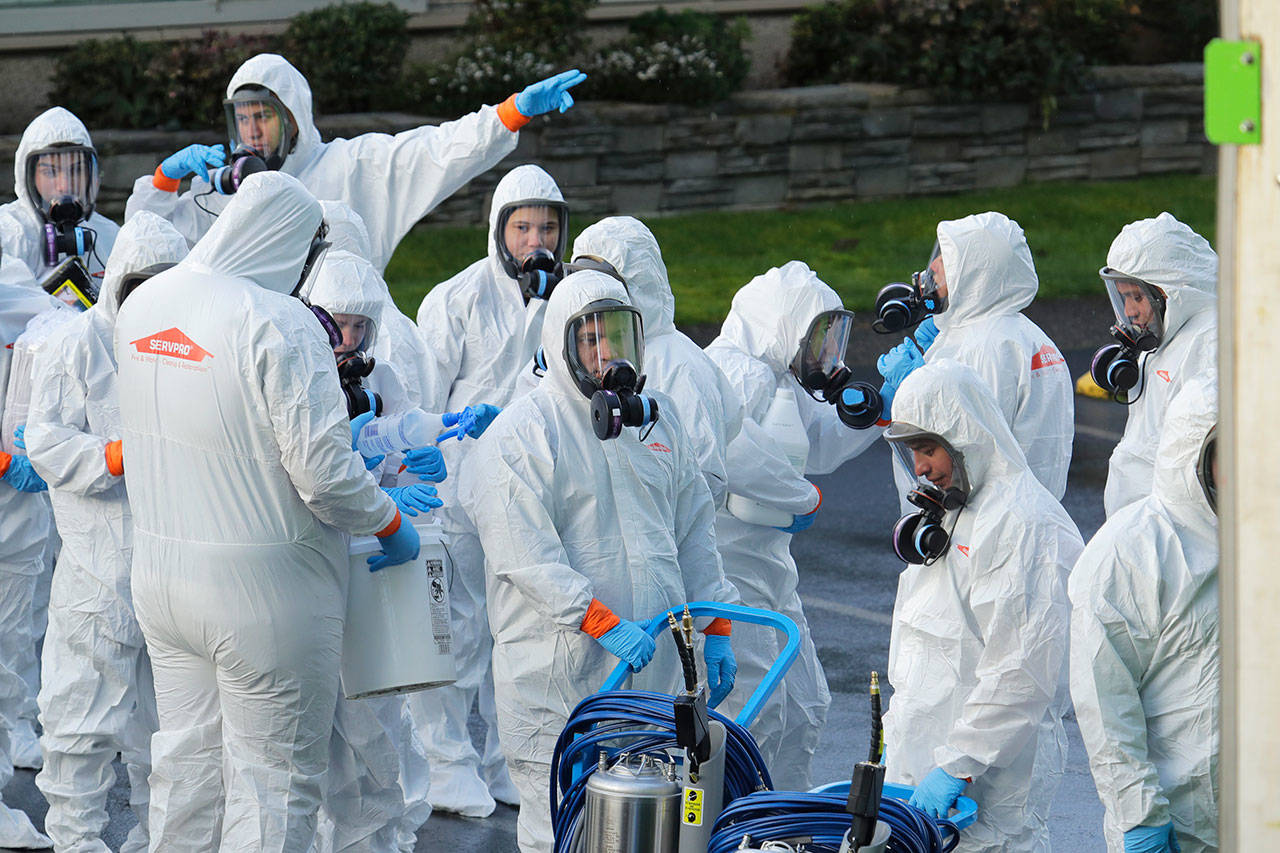 Workers from a Servpro disaster recovery team wearing protective suits and respirators enter the Life Care Center in Kirkland to begin cleaning and disinfecting the facility Wednesday, March 11, 2020, near Seattle. The nursing home is at the center of the coronavirus outbreak in Washington state. For most people, the virus causes only mild or moderate symptoms. For some it can cause more severe illness, especially in older adults and people with existing health problems. (Ted S. Warren/The Associated Press)