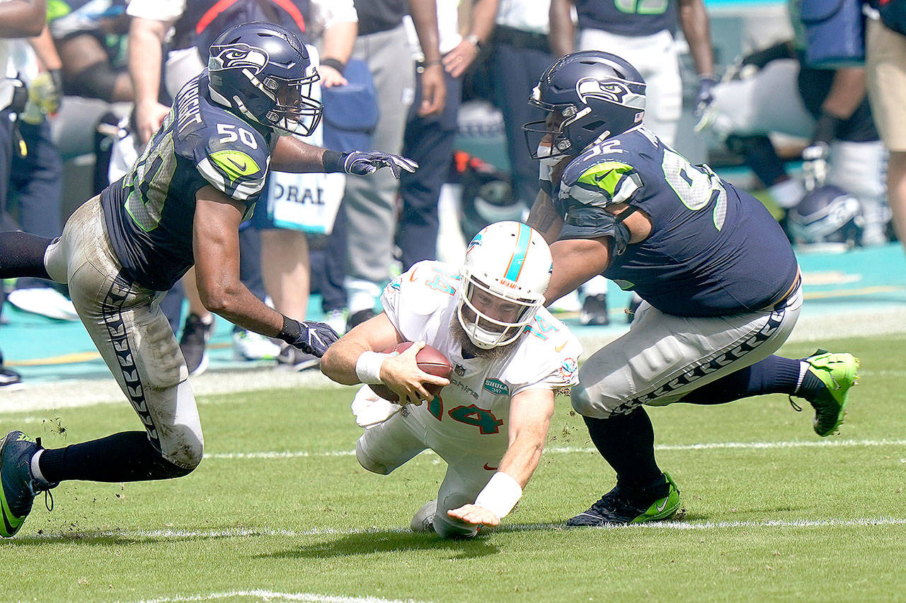 Miami Dolphins quarterback Ryan Fitzpatrick (14) falls as Seattle Seahawks outside linebacker K.J. Wright (50) and defensive tackle Bryan Mone (92) attempt to tackle, during the second half of an NFL football game Sunday, Oct. 4, 2020, in Miami Gardens, Fla. (Lynne Sladky/Associated Press)