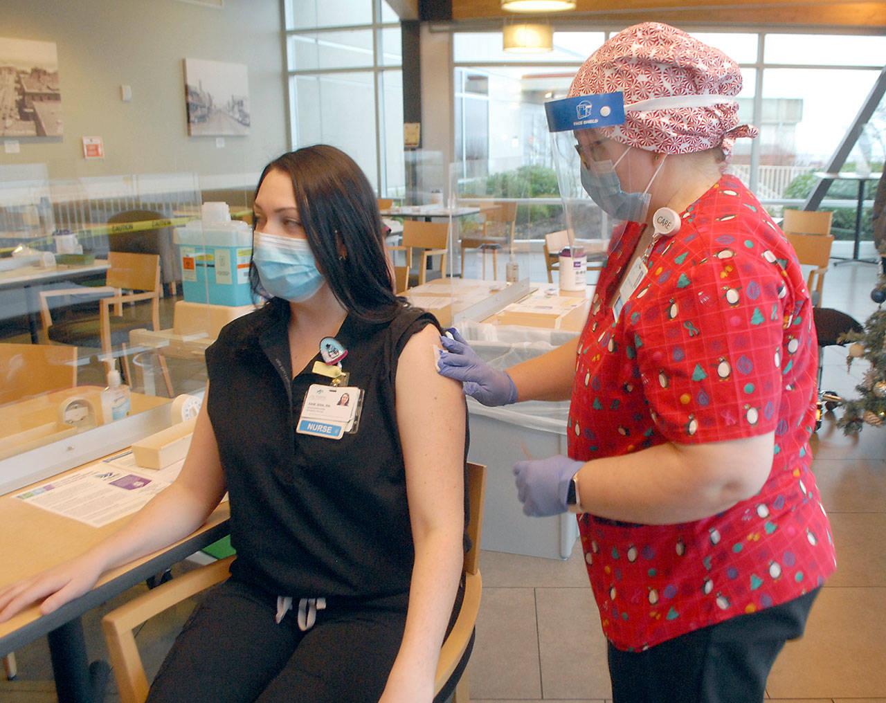 Registered nurse Gretchen Souza, director of education at Olympic Medical Center, right, applies a bandage to emergency services nurse Samantha Counts, who was the first person in Clallam County to receive a vaccination against COVID-19 during a clinic at the Port Angeles hospital Friday, Dec. 18, 2020. (Keith Thorpe/Peninsula Daily News)