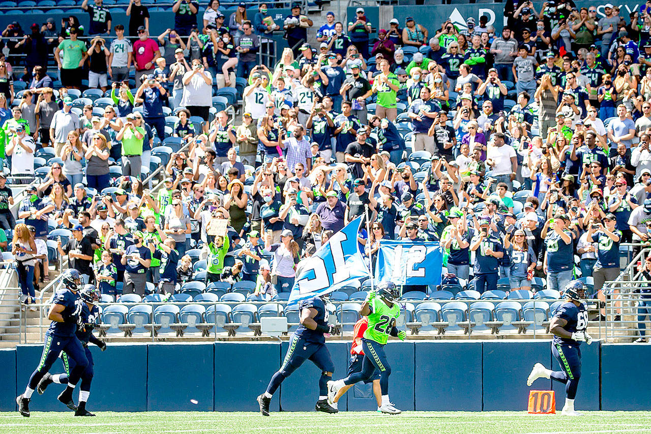 Seattle Seahawks cornerback Ugo Amadi carries the 12 flag out to cheering fans before playing a mock game as part of an NFL football training camp at Lumen Field in Seattle on Sunday. (Bettina Hansen/The Seattle Times via AP)