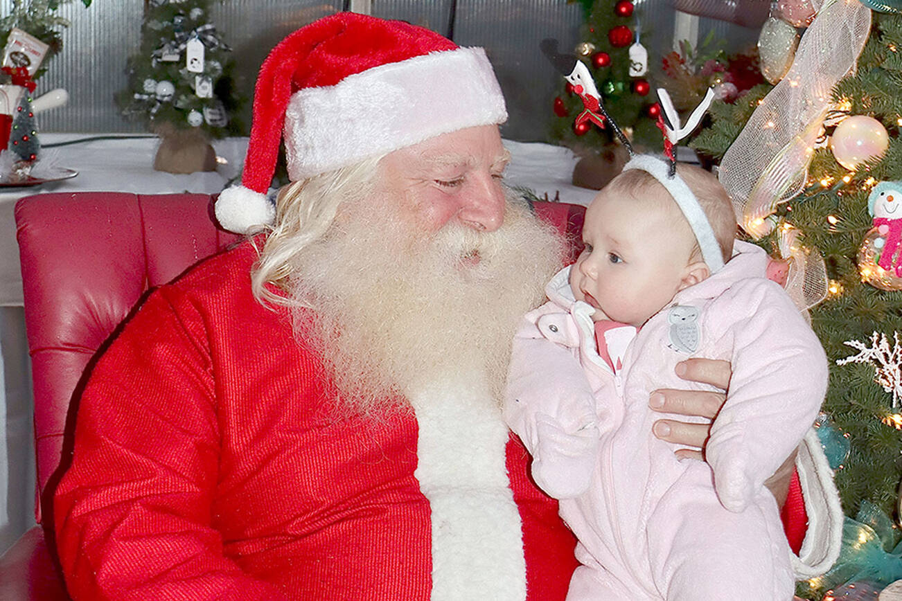 Barry Swegle plays Santa at the Candy Cane Christmas Cabin at The Answer for Youth (RAFY) Sprouting Hope Greenhouse as he holds 4-month-old Persephanie Svilar of Port Angeles. (Dave Logan/for Peninsula Daily News)