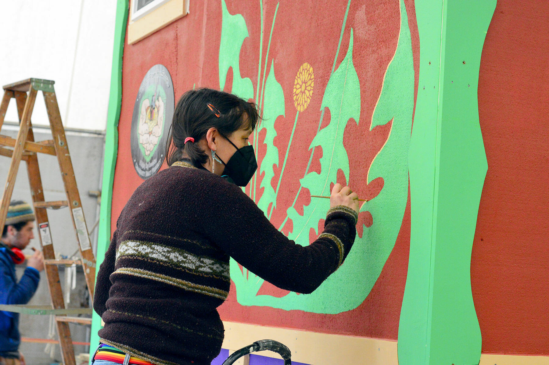 Muralist Danielle Fodor paints the newest tiny home, named Meadow Manor, at the Community Boat Project shop in Port Hadlock on Tuesday. The 160-square-foot home is an example of the housing to be built for farmworkers in Chimacum. (Diane Urbani de la Paz/Peninsula Daily News)
