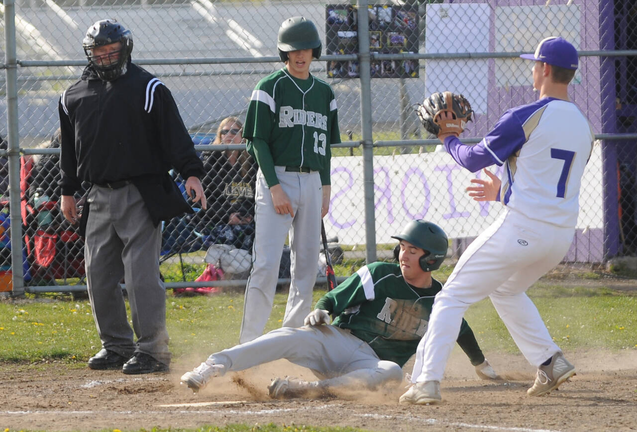 With teammate Hunter Robinson (13) looking on, Port Angeles’ Colton Romero slides safely into home ahead of the tag of Sequim pitcher Connor Bear in Sequim on Monday. (Michael Dashiell/Olympic Peninsula News Group)