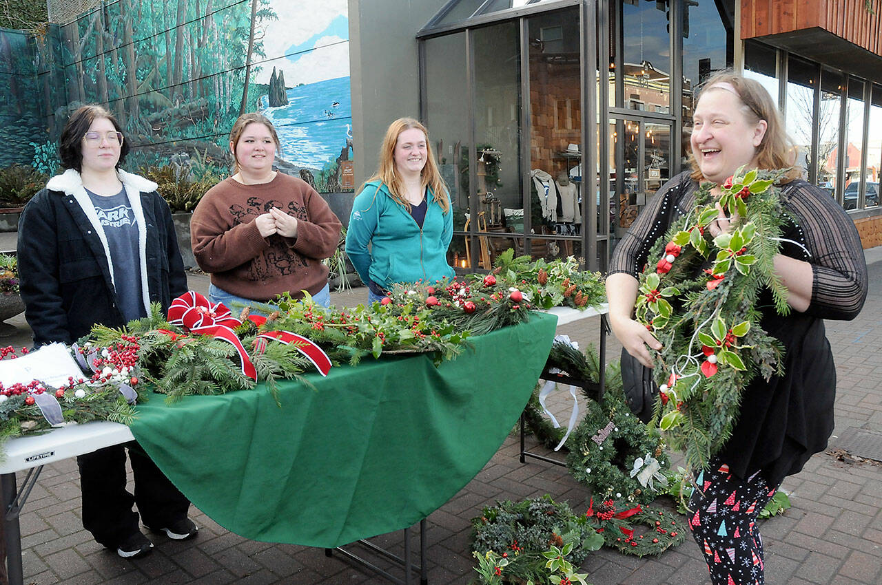 Louisa Monger of Port Angeles, right, shows off a handmade wreath she was purchasing at tables staffed by members of the Port Angeles High School Choir, including seniors, from left, Kaelyn Herringer, Rayna Mathison and Grace Possinger, on Saturday at the Conrad Dyar Memorial Fountain in downtown Port Angeles. The wreath sale was a benefit to help fund a spring trip to perform at Carnegie Hall in New York with members of the school’s choir, orchestra and band. Leftovers from Saturday’s sale, along with a bake sale and silent auction, will be available during the school’s holiday concert at 7 p.m. tonight at the Port Angeles Performing Arts Center, 304 E. Park Ave. (Keith Thorpe/Peninsula Daily News)