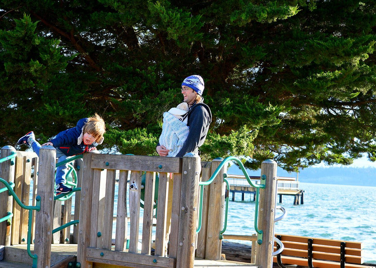 Roarke Jennings of Port Townsend, along with son Niko and baby Chiyo, take in the sun and wind at Pope Marine Park in downtown Port Townsend on Wednesday morning. (Diane Urbani de la Paz/For Peninsula Daily News)