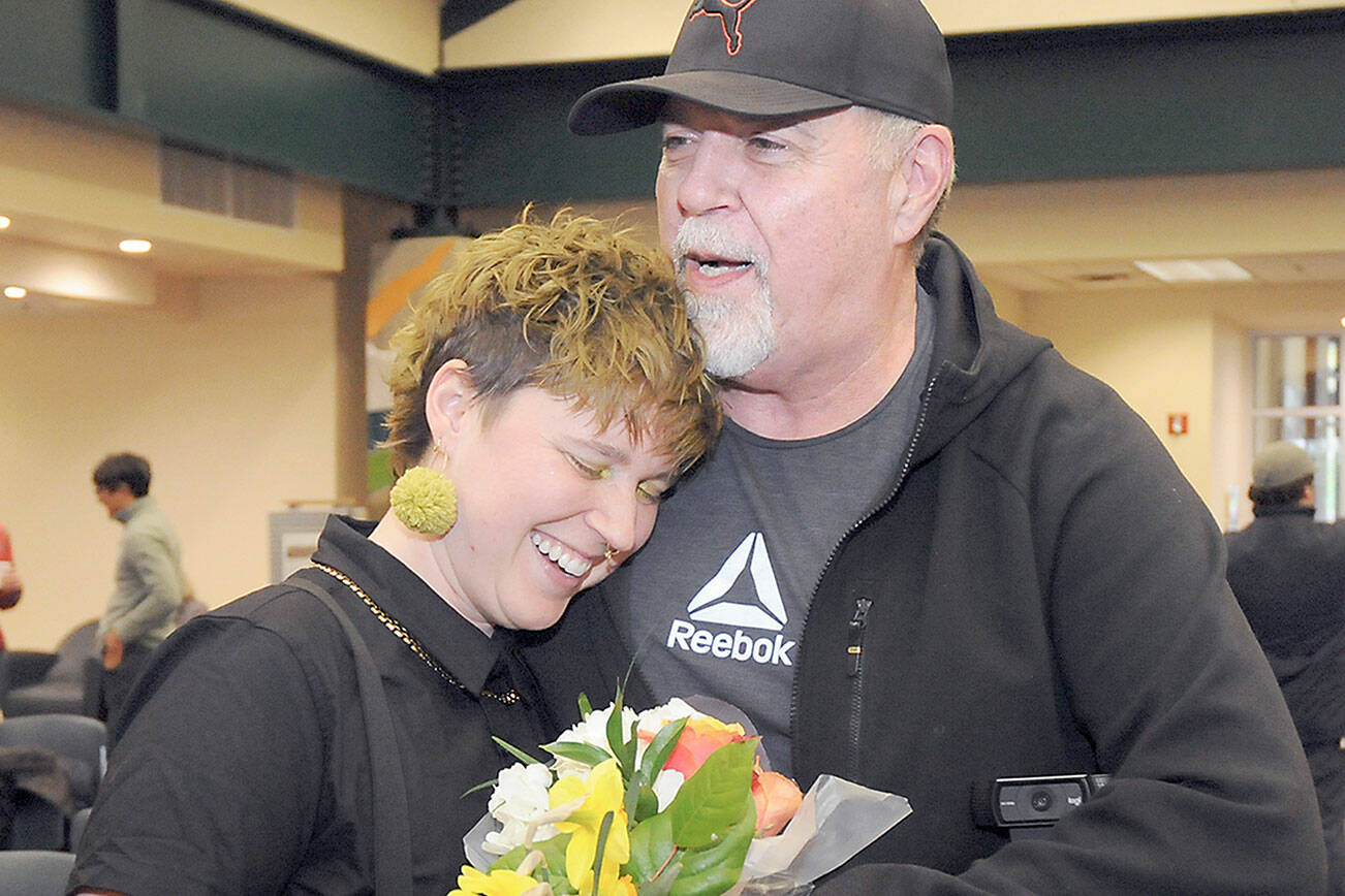 Jaiden Dokken, Clallam County’s first poet laureate, receives a hug and flowers from their father Mark Dokken of Port Angeles after Jaiden was inaugurated to their two-year post on Tuesday at the Port Angeles Public Library. (Keith Thorpe/Peninsula Daily News)