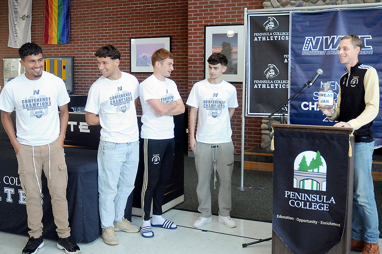 Peninsula College men’s soccer coach Jake Hughes, right, holds a gag “swear jar” poking fun of player Nil Grau, who used a number of swear words during an exuberant live-streamed postgame interview on Sunday after the team defeated Highline in the NWAC championship match on Sunday in Tukwila. The team was honored by the school at the Pirate Union Building on Tuesday. Next to the podium are players, from left, Manny Garcia, Konrad Muller, Pip van der Ende and Alfie Tucker. (Keith Thorpe/Peninsula Daily News)