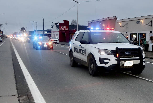 DAVE LOGAN/FOR PENINSULA DAILY NEWS A parade honoring Ron Cameron, with nearly two dozen vehicles with lights flashing, heads east on First Street in Port Angeles.