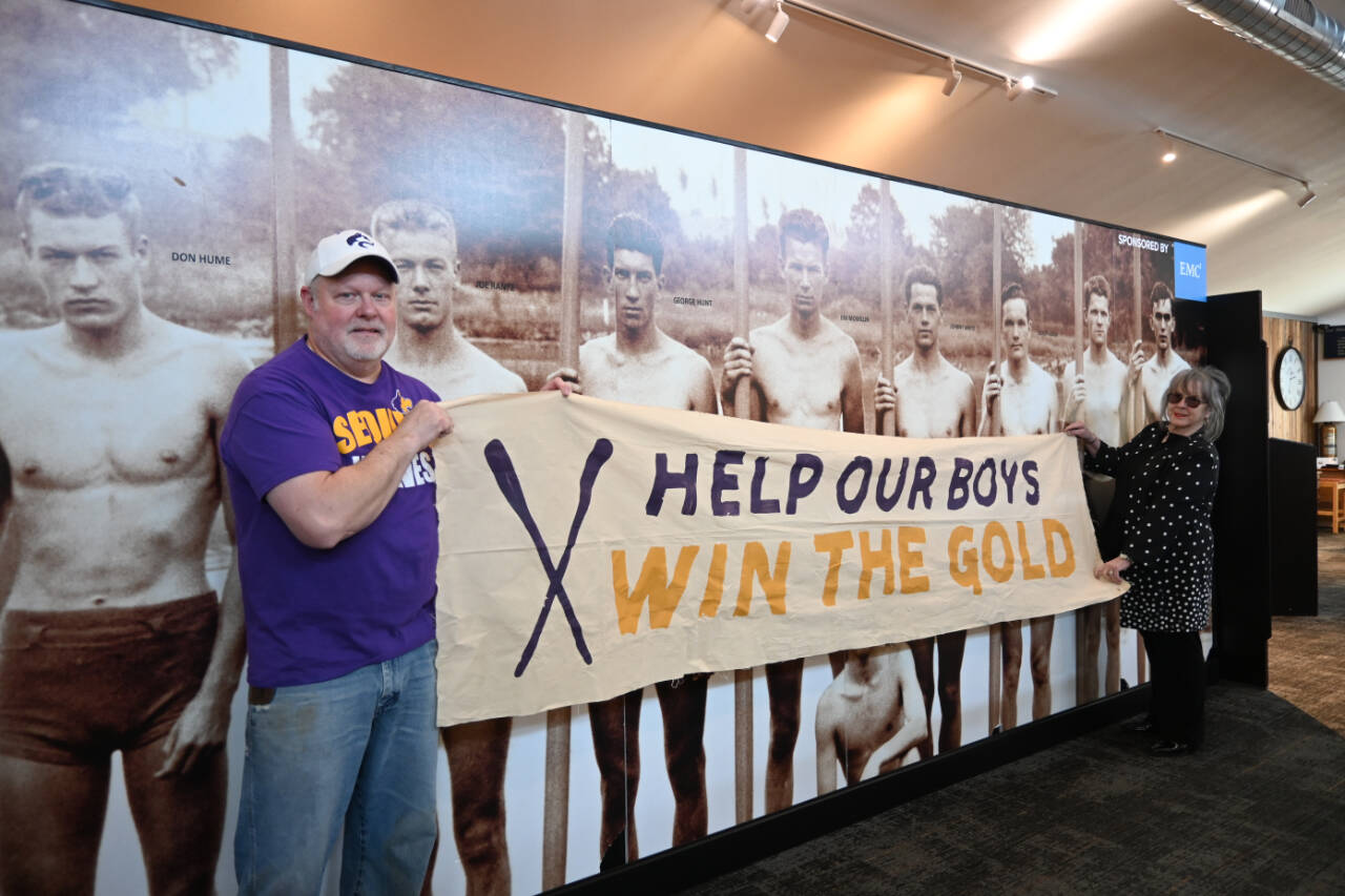 Randy Perry and Judy Reandeau Stipe, volunteer executive director of Sequim Museum Arts, hold aloft a banner from “The Boys in the Boat” film Perry purchased and is loaning to the museum. (Michael Dashiell/Olympic Peninsula News Group)