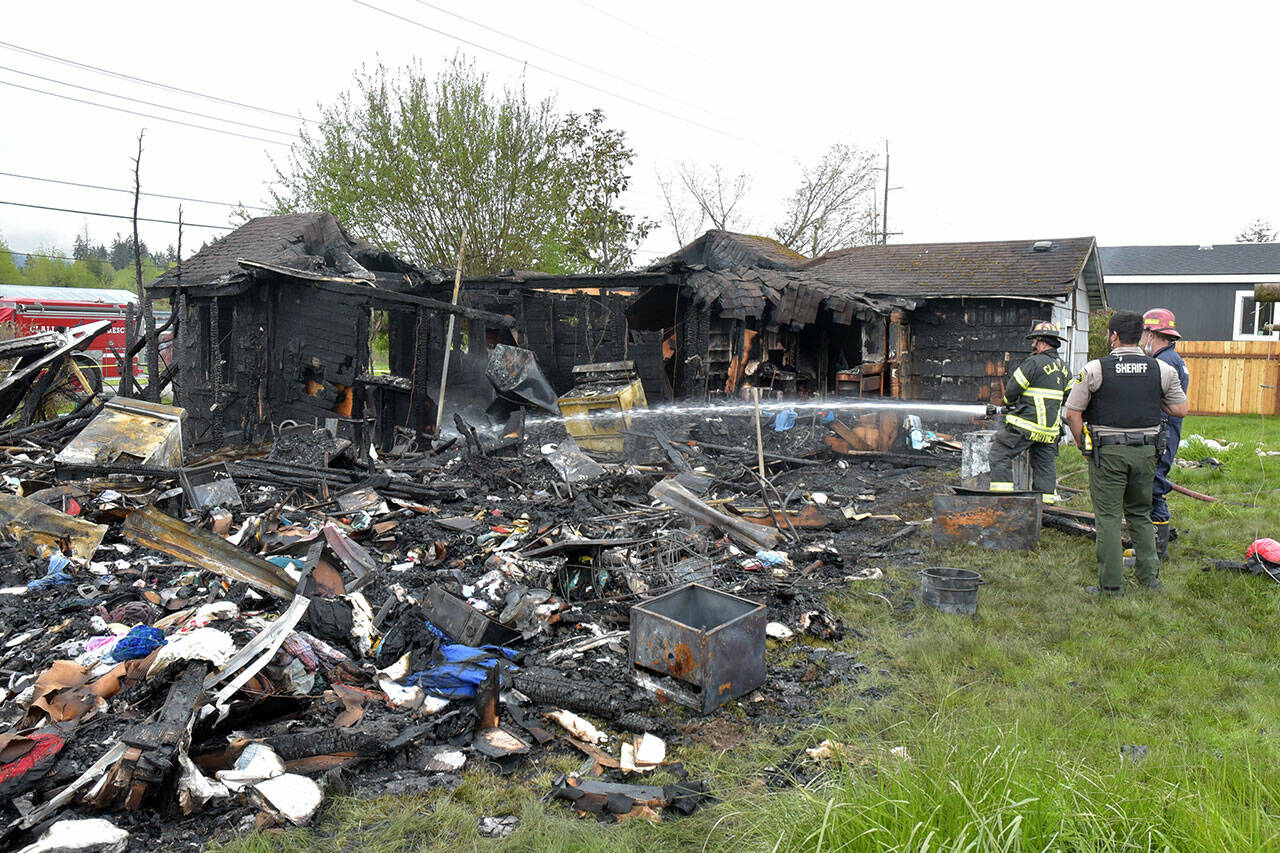 Clallam County Fire District Captain Marty Martinez sprays water on a hot spot of a fire that destroyed a house and adjoining RV in the 700 block of East Kemp Street near Port Angeles on Friday morning. (Keith Thorpe/Peninsula Daily News)