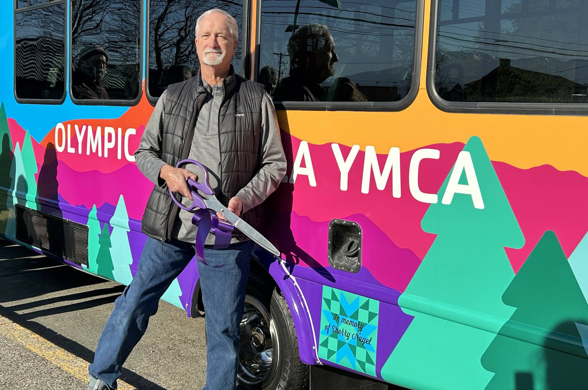 Mike Speer of Bonney Lake stands with the new bus his sister Sherry Nagel’s estate helped pay for at the YMCA of Sequim. A quilt square with a dedication to Nagel is on the side of the bus. (Matthew Nash/Olympic Peninsula News Group)
