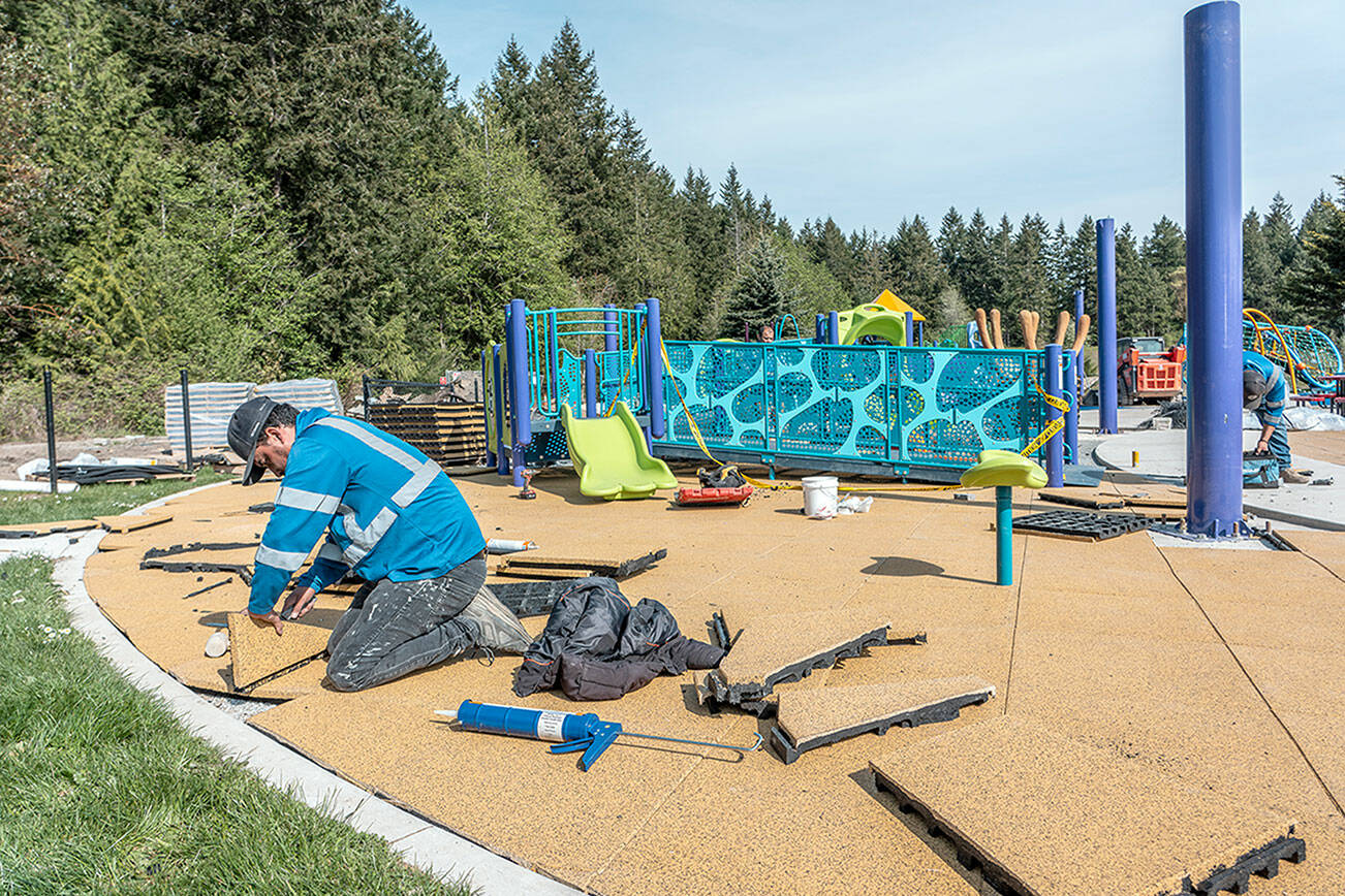 Manuel Sanchez, with MTZ Installs of Pasco, lays soft, foam tiles in the landing area of the JUMP playground area of HJ Carroll Park in Port Hadlock as part of phase two of new equipment and safety upgrades. (Steve Mullensky/for Peninsula Daily News)