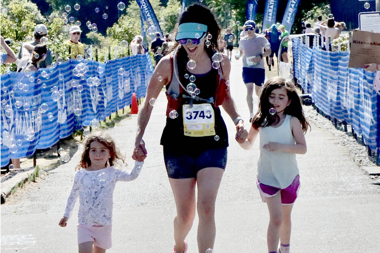Ivy Karlinsky of Seattle has her two daughters Isla, 6, and Ellie, 3, help her over the finish line during the last 20 meters of her half-marathon race at the Port Angeles Pier on Sunday. (Dave Logan/for Peninsula Daily News)