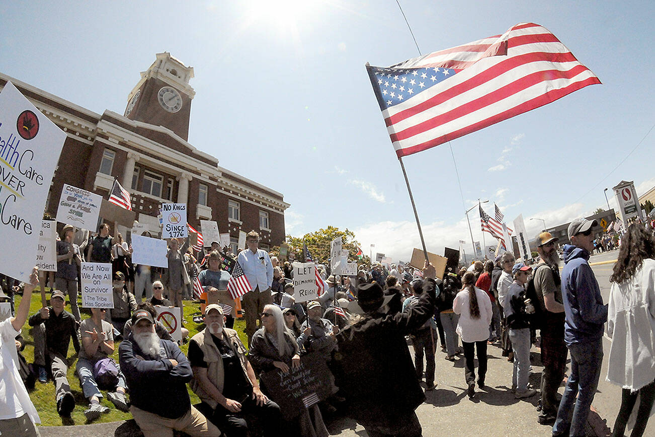 A demonstrator carrying an American flag walks the sidewalk in front of the Clallam County Courthouse on Saturday. (Keith Thorpe/Peninsula Daily News)