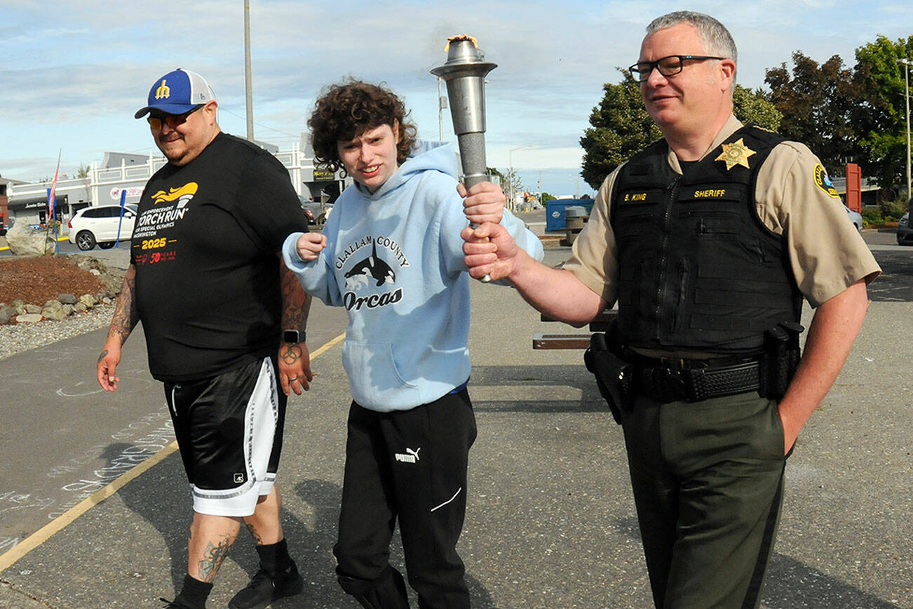 Special Olympian Deni Isett, center, holds a ceremonial torch with Clallam County Sheriff Brian King, right, accompanied by Lt. Jim Thompson of the Lower Elwha Klallam Tribal Police on a leg of the Law Enforcement Torch Run on the Olympic Discovery Trail at Port Angeles City Pier. Tuesday’s segment of the run, conducted mostly by area law enforcement agencies, was organized to support Special Olympics Washington and was to culminate with a community celebration at 7 Cedars Casino in Blyn. (Keith Thorpe/Peninsula Daily News)