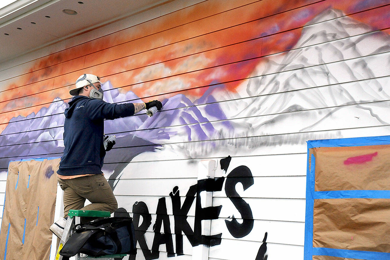 Muralist Adam Nelson of Port Angeles paints a mountainscape on the north wall of Drake’s U-Bake Pizza & Subs on Wednesday in Port Angeles. Nelson said the job would take about two days to complete. (Keith Thorpe/Peninsula Daily News)