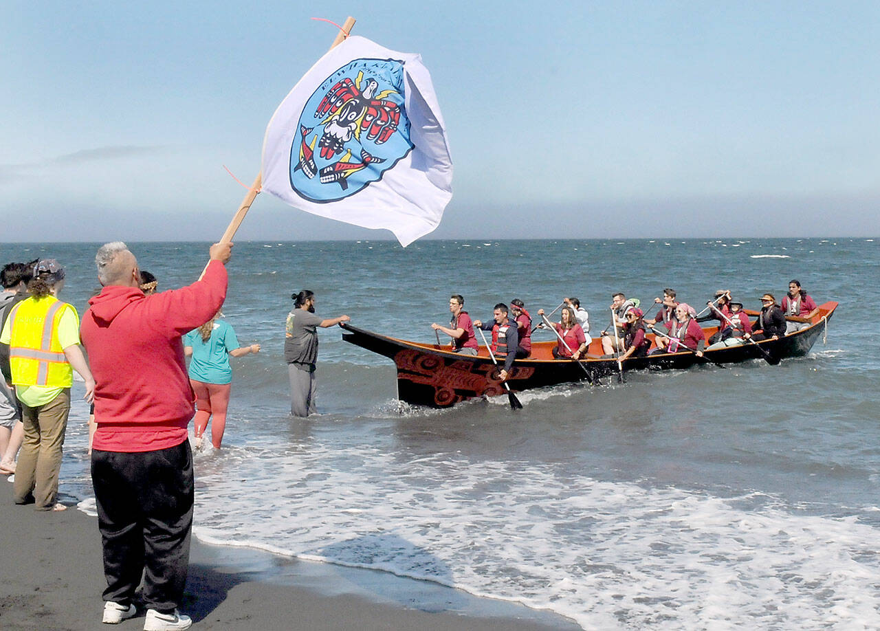 Tribal member Jerry Foster waves a Lower Elwha Klallam tribal flag as a canoe paddled by members of the Port Gamble S’Klallam Tribe arrives at Elwha Beach at Angeles Point on Thursday. (Keith Thorpe/Peninsula Daily News)