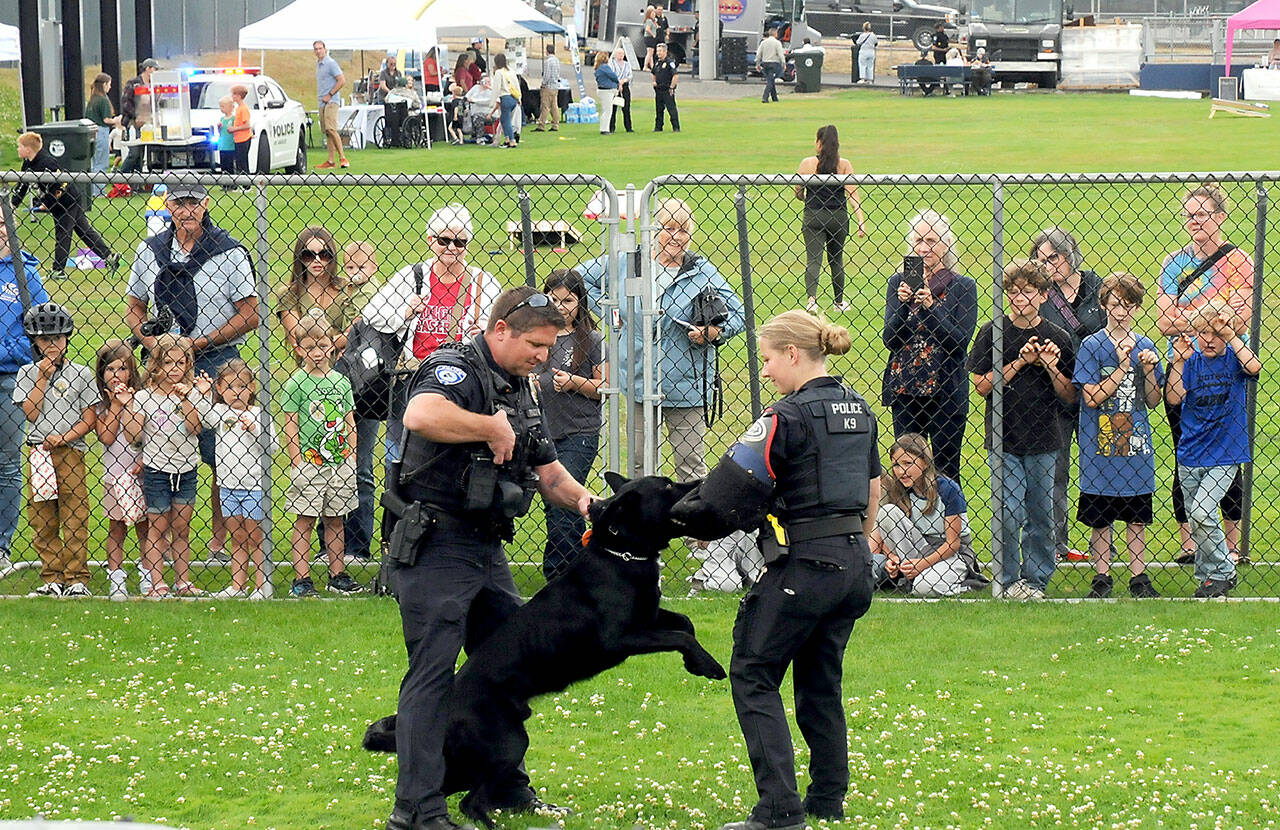 Port Angeles Police officers Kenneth McKnight, left, and Lilliana Emery give a canine demonstration with Freddy, a trained police dog, during Tuesday’s National Night Out at Port Angeles Civic Field. The nationwide event brought law enforcement agencies, watch groups and civic organizations together for an evening of community building, featuring informational displays, children’s activities and a large-screen movie presentation. (Keith Thorpe/Peninsula Daily News)