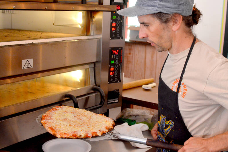 Flutter By Pizza Pie owner and operator Mark Ennis pulls a cheese pizza from the oven. (Elijah Sussman/Peninsula Daily News)