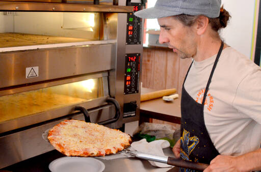 Flutter By Pizza Pie owner and operator Mark Ennis pulls a cheese pizza from the oven. (Elijah Sussman/Peninsula Daily News)