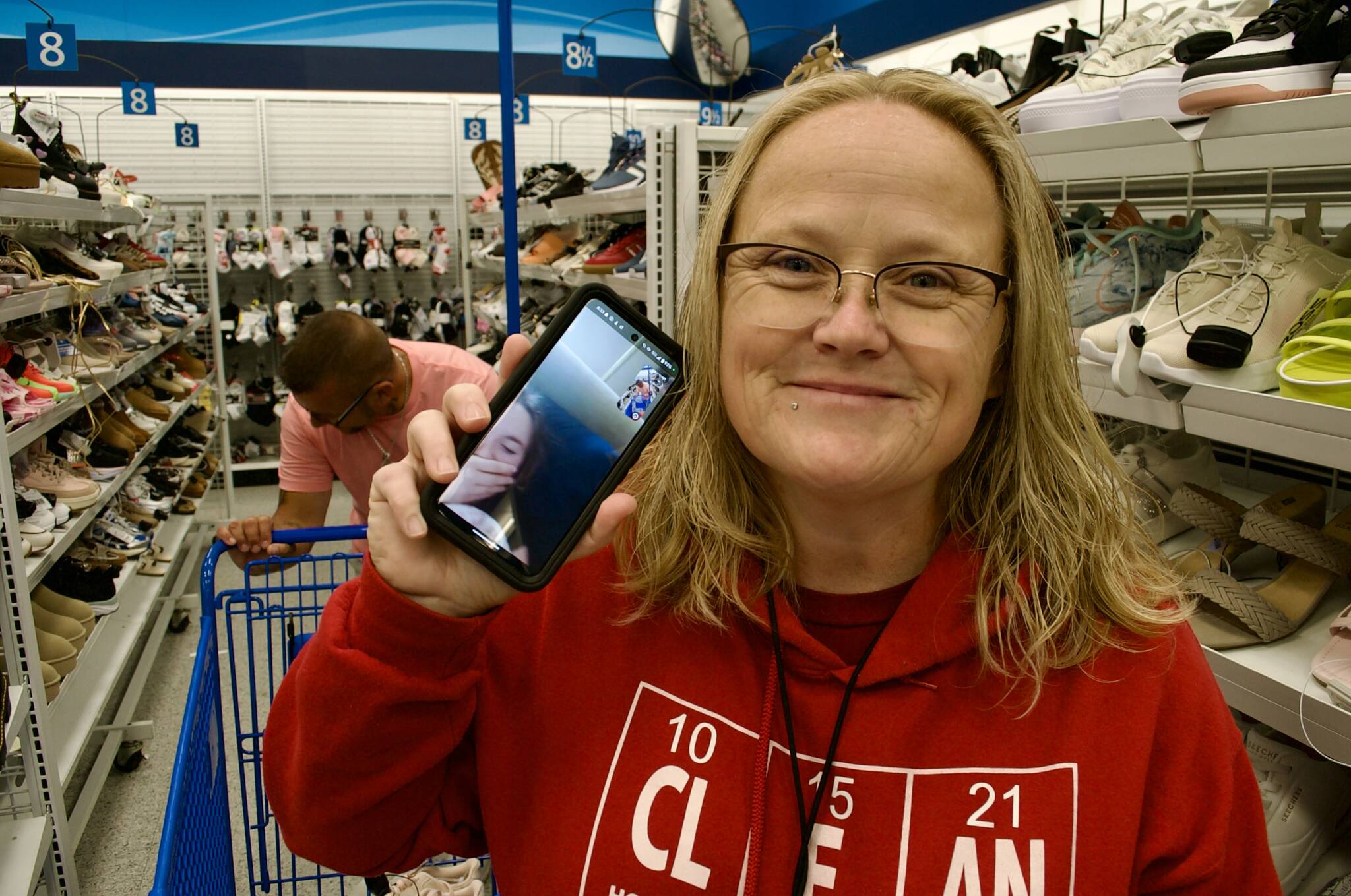 Tammy Blessing holds up her cell phone through which she is communicating with her daughter, Taylor White. She and her husband Cassidy Blessing (behind her) shop for a new pair of school shoes for Taylor with a gift card provided by H.U.M.A.N., a new Sequim nonprofit created by Cassidy’s former bosses, Darrin and Alicia Liggins. (Jacques Star/Olympic Peninsula News Group)