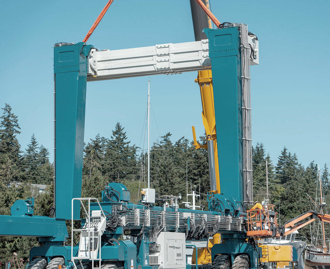 Still suspended and held in steady by a heavy lift crane, a 50-ton crossmember beam of the new 300-ton variable width Travelift acquired by the Port of Port Townsend is bolted down by an employee, lower right, on Monday. (Steve Mullensky/for Peninsula Daily News)