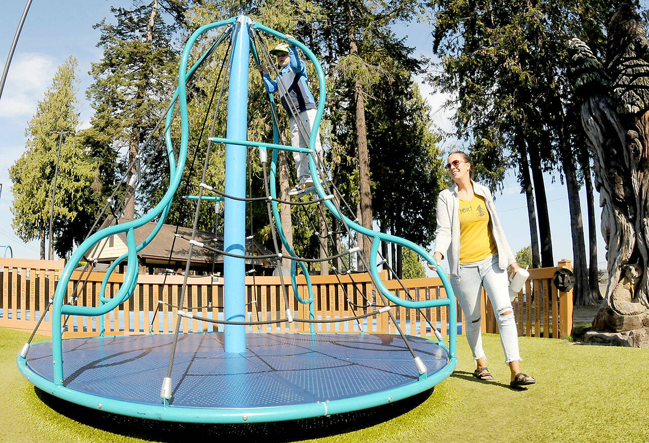 Carlyn Beebe of Forks pushes a merry-go-round toy as her son, Lane, 6, takes a ride on Tuesday at the Dream Playground at Erickson Playfield in Port Angeles. The pair took time out from errands for a visit to the popular park. (Keith Thorpe/Peninsula Daily News)