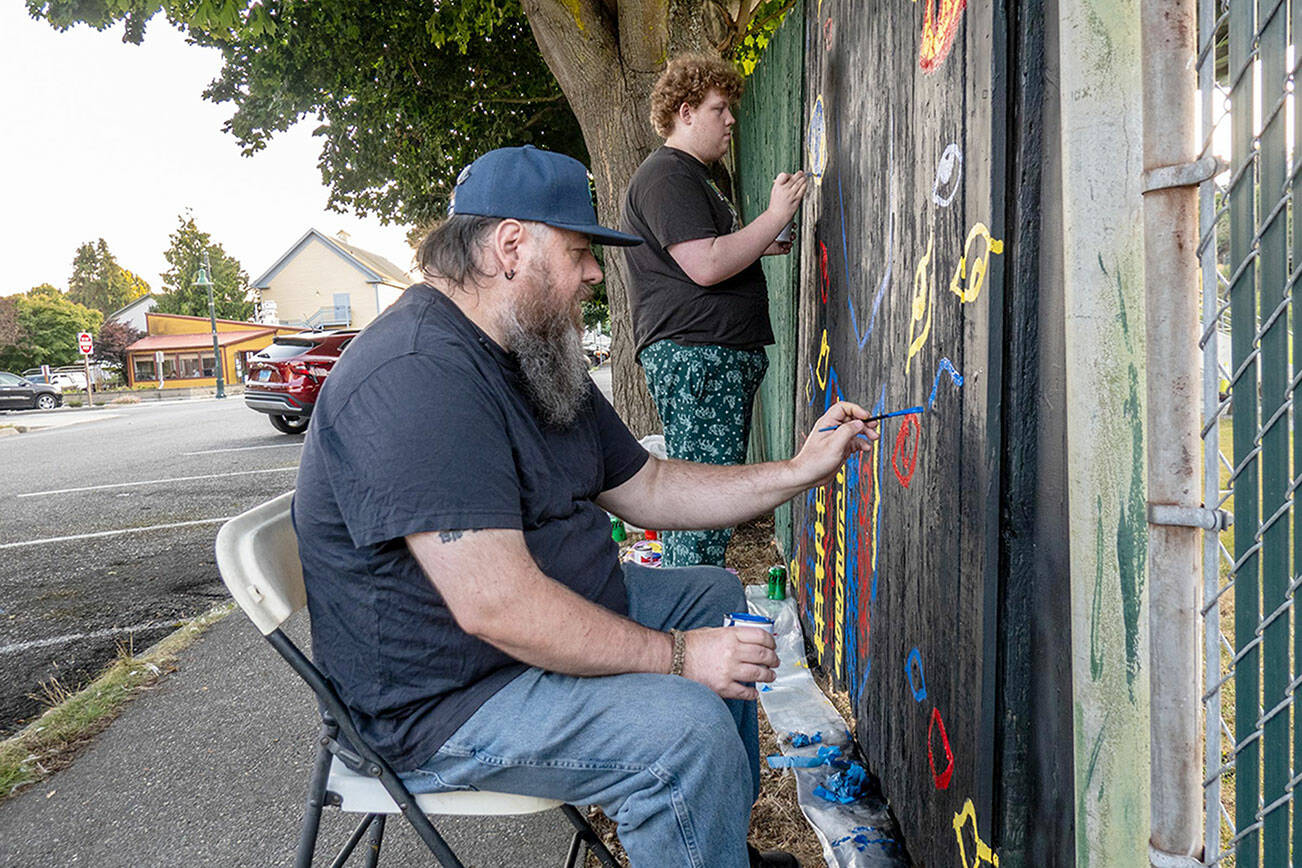 Jesse Adams, front, of Port Townsend, and son Evan of Allyn paint eyes on a section of the fence surrounding Port Townsend’s Memorial Field as their contribution to the Outsiders Street Art Project Port Townsend during Jefferson County’s first community public art project. Adams’ project, titled “Eye Strain,” had to be submitted for approval before work could begin. Each artist had an 8-foot section of fence to work on. The fence will be taken down, most likely next spring, to be replaced with a new one. (Steve Mullensky/for Peninsula Daily News)
