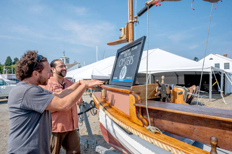 Ralph Riccio, left, of Port Townsend, checks the level of the sign for his setup at the Wooden Boat Festival at the Point Hudson Marina on Wednesday afternoon. Riccio raises oysters on his farm, Marrowstone Island Fresh Oysters, in Kilisut Harbor, between Indian Island and Marrowstone Island. The festival opens at 9 a.m. Friday with a free preview after 5 p.m. today. (Steve Mullensky/for Peninsula Daily News)