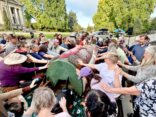 A crowd of about 120 people bless a totem pole and 10 cedar masks carved by the Lummi Nation’s House of Tears outside of the Capitol building in Olympia on Monday as part of the Indigenous-led campaign “Xaalh and the Way of the Masks.” The totem and masks will travel 1,700 miles between rally sites in Washington and Oregon before it’s given to the Lower Elwha Klallam Tribe west of Port Angeles on Sept. 20. (Emily Fitzgerald/Washington State Standard)