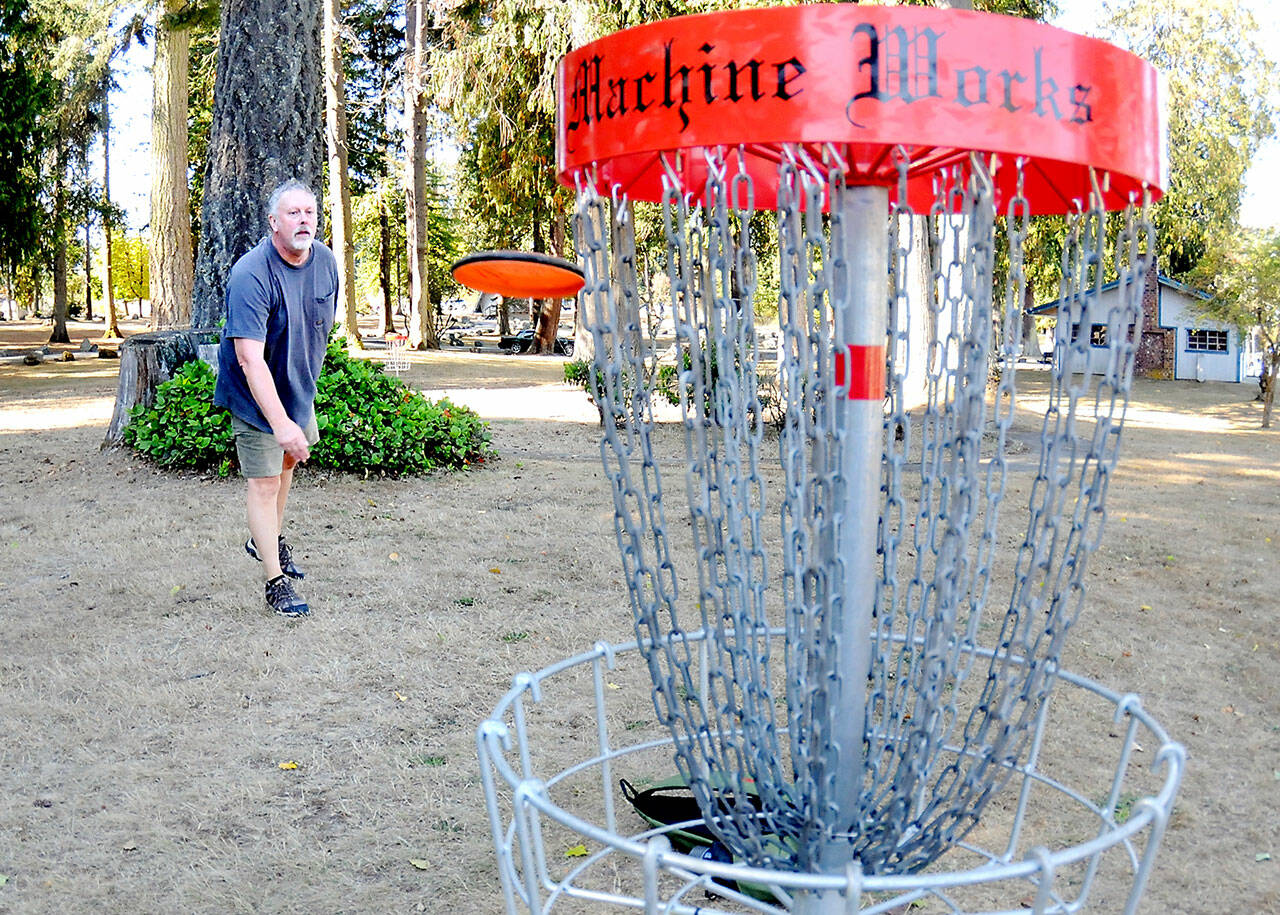Michael Thill of Boquete, Panama, formerly of Sequim, practices his putts at the disc golf course on Thursday at Lincoln Park in Port Angeles. The park features a full 18-hole course for disc golf enthusiasts. (Keith Thorpe/Peninsula Daily News)