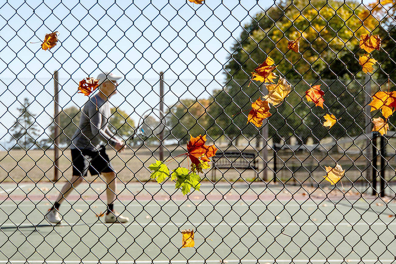 Fallen leaves cling to a fence as Chris White of Port Townsend sets up for a forehand volley during a tennis match at the Fort Worden tennis courts on Thursday. (Steve Mullensky/for Peninsula Daily News)