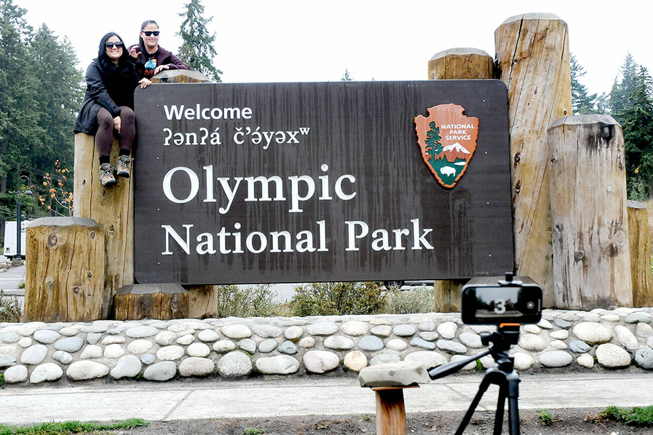 Lorena Miramontes Morley, left, and her spouse, Mandy Miramontes Morley, both of Anaheim, Calif., use a remote-controlled camera to take a self-portrait on the Olympic National Park entrance sign on Tuesday in Port Angeles. (Keith Thorpe/Peninsula Daily News)