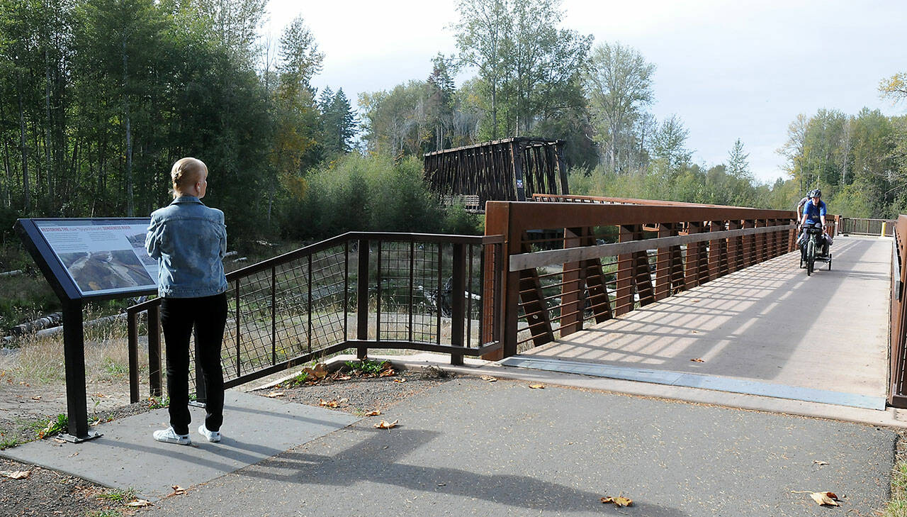Josette Goarin of Sequim pauses at an informational kiosk as she watches a pair of bicyclists approach over a span connecting the railroad bridge to the Olympic Discovery Trail on Friday near the Dungeness Nature Center at Railroad Bridge Park in Sequim. The popular park and nearby nature center offer a glimpse of the Dungeness River watershed and provide a venue for outdoor leisure activities. (Keith Thorpe/Peninsula Daily News)