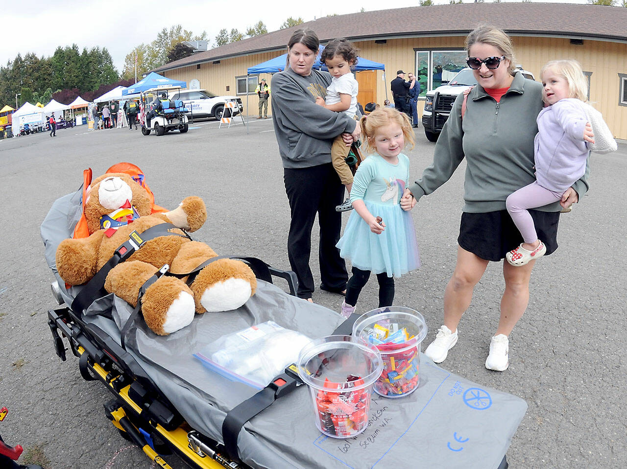 Gabriella Wolman, holding her son, Andy Wolman, 2, left, and Francesca Wolman, with daughters Lily Parker, 5, and Lucy Parker, 2, all of Sequim, examine a gurney with a stuffed bear placed on display by Olympic Ambulance during Saturday’s Safety Fair at Carrie Blake Park in Sequim. The fair, hosted by the city of Sequim, Clallam County Fire District 3 and members of the Community Emergency Response Team, featured a variety of public safety displays and demonstrations as well as workshops and lectures themed around surviving an emergency. (Keith Thorpe/Peninsula Daily News)