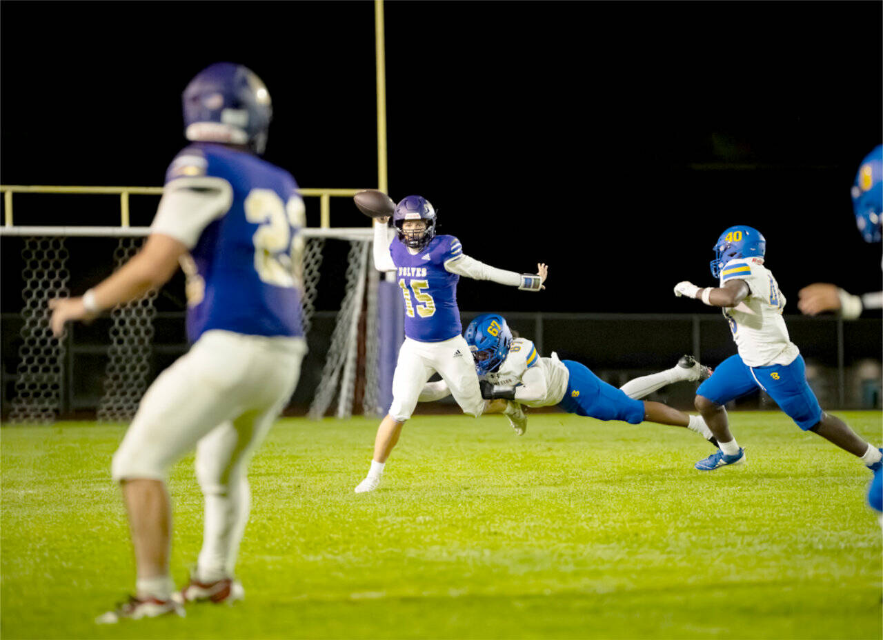 Sequim quarterback Kaden Miller (15) evades a Bremerton tackle as he tries to get a pass off to teammate Patrick Elias (22) on Friday night in Sequim. Bremerton won the game 34-12. (Diamond Gentile/for Peninsula Daily News)