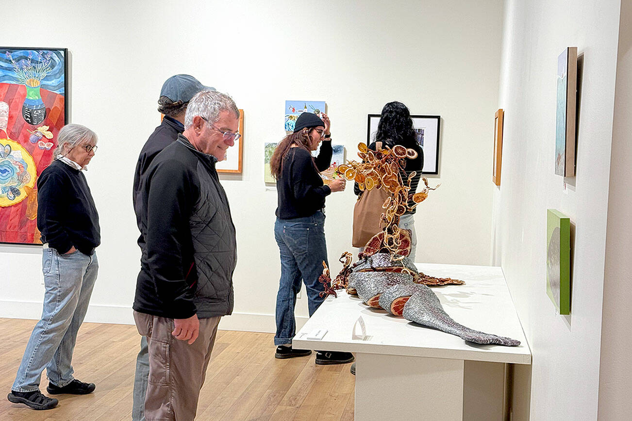 Jeanette Best Gallery visitors check out Ali Whitmore’s “Entree — Stuffed Whole Trout” during Art Walk. The sculpture won the Jurors’ Choice and People’s Choice awards in the recent “Potluck Banquet” exhibition. (Diane Urbani/Northwind Art)