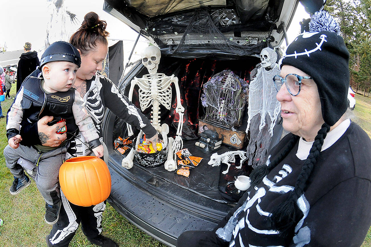 Jessica Topham of Sequim collects sweet treats for her son, Ivar Baker, 19 months, as Becky Rice looks on from her spookily decorated vehicle during Saturday’s Country Fair and Trunk or Treat at the Sequim Prairie Grange north of Carlsborg. The Halloween-themed event featured food, games, pumpkin carving and scary treats, hosted by members of the grange. (Keith Thorpe/Peninsula Daily News)