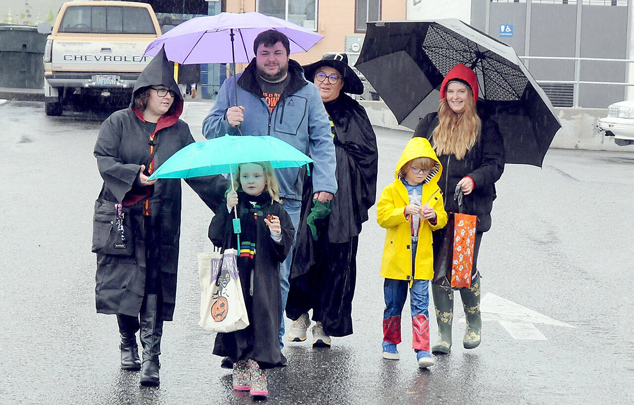 Trick or treaters and parents, from left, Angelina Simpson, Charlie Simpson, 6, Matt Simpson, Carmen Moody, Maximillion Dempsey, 7, and Holly Dempsey, all of Port Angeles, make their way through downtown Port Angeles under a moderate rain shower on Halloween Day. Many downtown merchants opened their doors with candy and treats to welcome soggy spooks, wet witches and other assorted cartoon characters in search of sweet snacks. (Keith Thorpe/Peninsula Daily News)