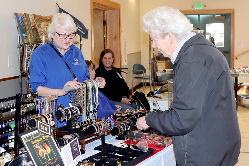 Gwyn Gallis, left, helps Pauline Olsen at the Soroptimist booth at the Port Angeles Senior and Community Center during a holiday craft fair on Saturday. Soroptimists were even selling their annual Elegant Gourmet Coupon Book for $10. They can also be purchased at Blackbird Coffee House, Fogtown Coffee Bar, Jim’s Pharmacy, Odyssey Book Store, Sweet Spot Sequim and Sequim Shoe Repair. More than a dozen vendors filled the building for holiday shoppers. (Dave Logan/for Peninsula Daily News)